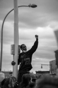 Black man with fist in the hair holding on to light post at Black Lives Matter Protest