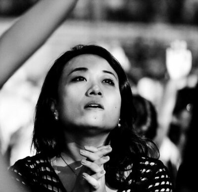 Black and white photograph of woman looking up, her hands clasped.