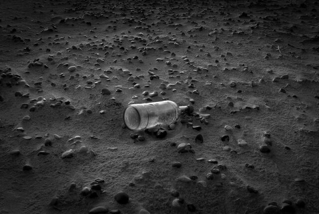Black and white photograph of a bottle on a beach.