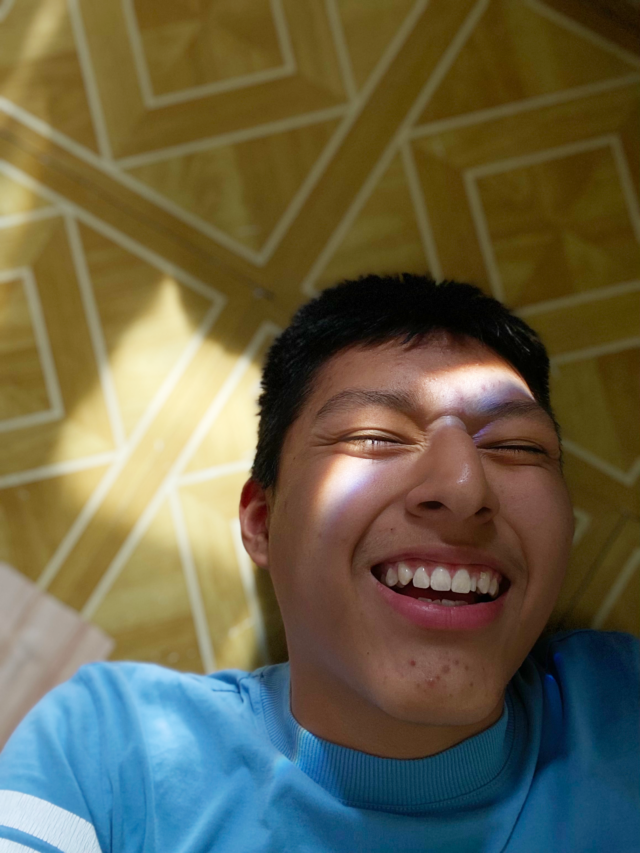 Image of young man on a yellow patterned linoleum tile floor with a prism of light on his face.